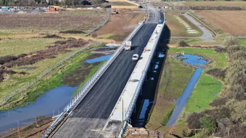 An aerial photograph showing fresh tarmac on a road bridge which crosses wetlands