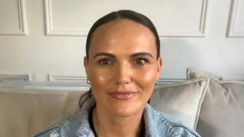 Caroline is looking and smiling at the camera. Her hair is tied back. 