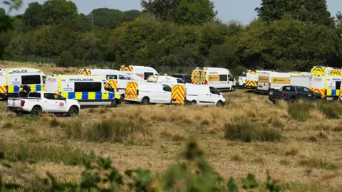 Eddie Mitchell A line of police vehicles and other emergency vehicles on a field.