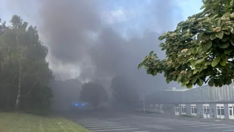 Shropshire Fire and Rescue Service Clouds of smoke billow through the area near the fire and through the smoke factory buildings can be seen as well as blue lights from emergency vehicles.
