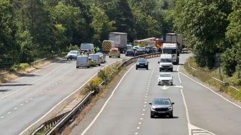 Emergency services including police and firefighters at the scene of a crash on the A38 in Devon. Several other cars, vans and lorries are on the road.
