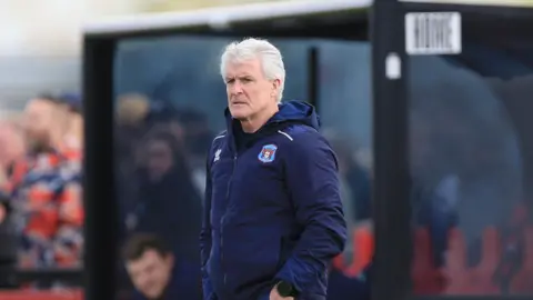 Mark Hughes in his Carlisle hooded jacket, stood on the touchline at Truro 