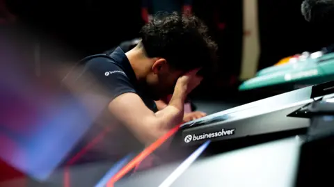 Formula One Otis Lawrence sat with his head in his hands. He is sitting in front of a desk.