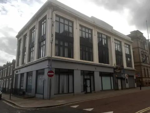 Arngrove House. It is a large three storey building with wide and long windows, grey render at the bottom and cream on the top two floors.