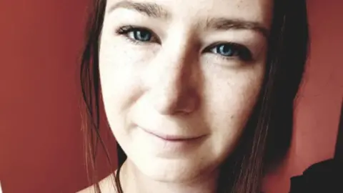 May De Malpas Finlay May De Malpas Finlay, who has brown hair and blue eyes, smiling very closely to the camera with a red background