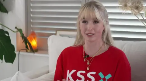 A blonde woman wearing a red jumper with Air Ambulance Charity Kent Surrey Sussex written on it. 