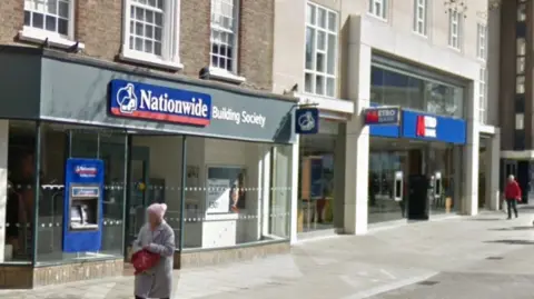 Google The Nationwide Building Society branch in Peterborough city centre. It is in a pedestrianised street and has a glass front. It is next to a Metro bank.