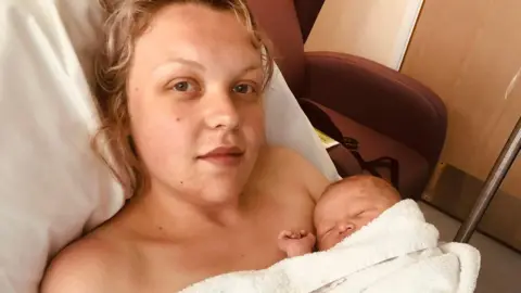 Annie Tombs lying in a hospital bed after giving birth to her son, who is wrapped up in a blanket and lying on her chest.