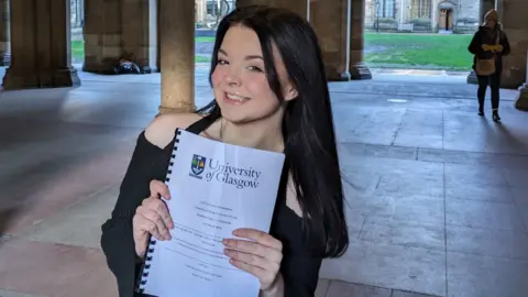 Regan holding her dissertation at Glasgow University