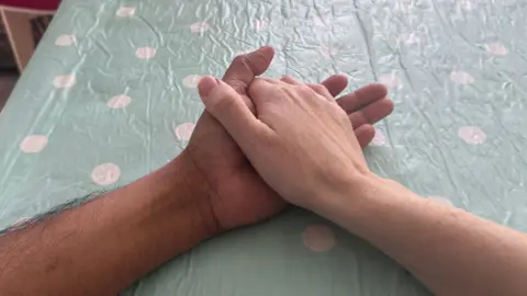 BBC Two arms from two different people resting on a table with a blue and white spotted tablecloth with hands interlinked