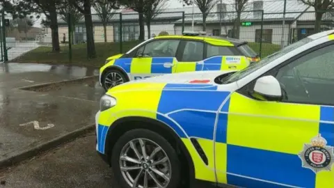Two States of Jersey police cars parked outside the school. There is a number 2 painted on the pavement.