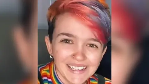 Family handout Imogen Nunn looks at the camera and smiles. She has red streaks in her hair and is wearing a rainbow striped top. Her nose is pierced.
