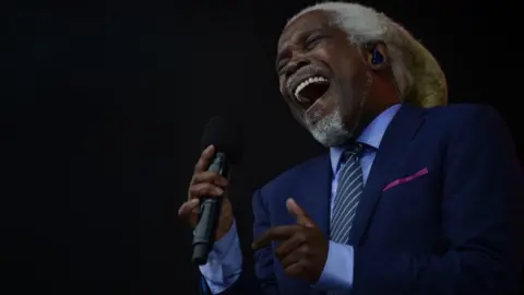 BBC Billy Ocean with long white hair holding a microphone and laughing