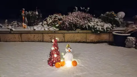 Airthrey Princess/BBC Weather Watchers A little snowman built in a garden, next to a very small Christmas tree