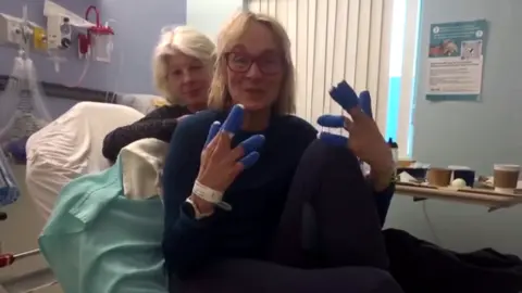 Louise Minchin/Instagram Louise Minchin holds up her bandaged hands while lying in a hospital bed.