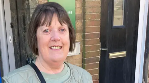 Local Democracy Reporting Service A woman with dark hair and a light green top is on the left of the photo looking at the camera. A black door is on the right.