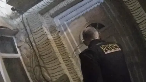 A police officer from City of London Police stands outside a house