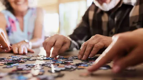 Close up of unrecognisable group of people playing with jigsaw puzzles at a care home.
