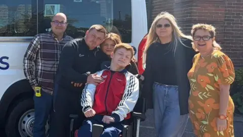 Shorefields School A group picture of school deputy head teacher Ryan Bruce and head teacher Gemma Fowler with Ralph's parents, brother and sister. They are all looking pleased in front of a white minibus.