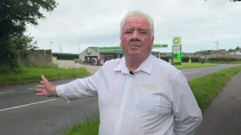 Peter Gaston pointing at a BP garage on the other side of the road.