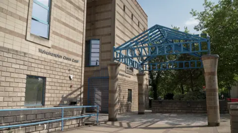 The entrance to Wolverhampton Crown Court. A blue metal frame is above the main door, with blue railings to the left of the shot.
