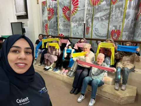 A woman smiling in a selfie with a group of women holding exercise bands