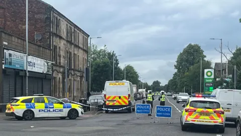 A police scene in Paisley - there are vans, police cars and ROAD CLOSED signs across the area, and officers in high vis vests standing at the scene