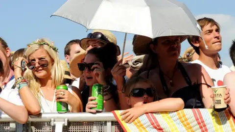 People standing in a crowd wearing sunglasses and holding a silver umbrella. 