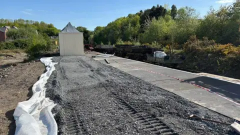 Josh Hall A large quantity of gravel leading to a railway platform and a small white building