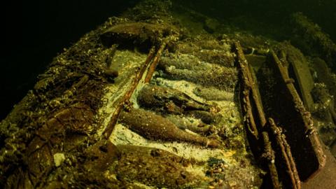 A shipwreck on the bottom of the sea in which old champagne bottles can be seen in the middle
