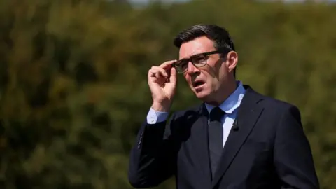 Reuters Prime Minister Andy Burnham talking while adjusting his glasses