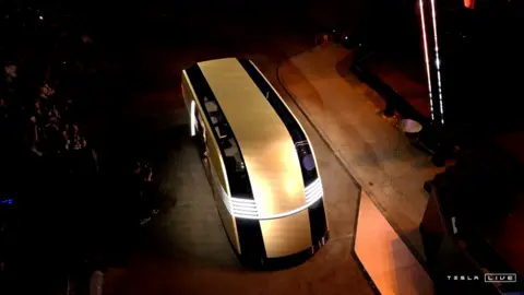 Tesla/Reuters Uno screenshot dal live streaming di Tesla mostra l'elegante Robovan dorato e nero illuminato mentre avanza nel mezzo della presentazione. 