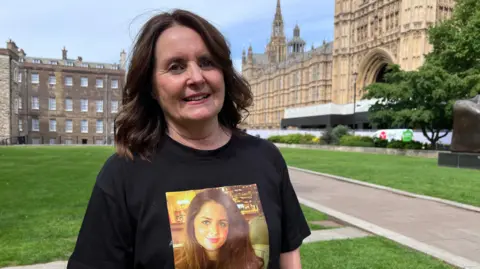Jess has shoulder length dark brown hair. Her t-shirt has a photo of her late daughter on it.