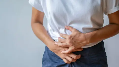 A young woman holding her lower abdomen, in pain due to cramps or a stomachache.