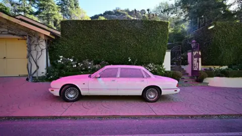 A white car in Los Angeles County covered in pink powder. It is fire retardant - a mixture of chemicals used to suppress wildfire growth. 