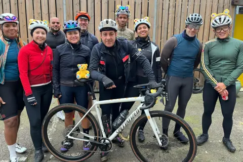 Nico Georgiou Nico Georgiou (centre) leans on his bike with Pudsey bear on the saddle alongside nine other cyclists, some of whom are wearing Pudsey ears