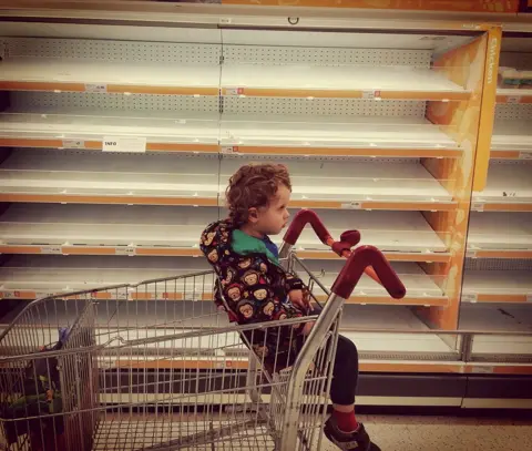 Julie Thiberg Child next to empty shelves in supermarket