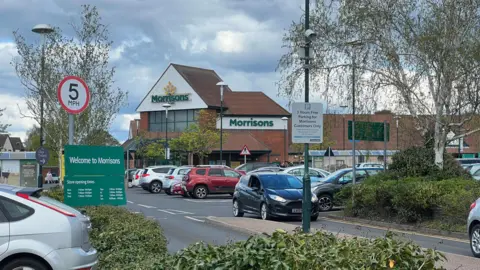 The Morrisons store in Aldridge, where Sean Egan worked for 29 years before his dismissal. A protest is planned outside the supermarket on Saturday morning. Cars fill the car park beneath a cloudy sky.