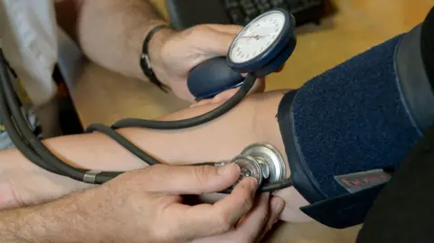Close-up of a healthcare worker measuring a person's blood pressure using a cuff, gauge and stethoscope during a health check.