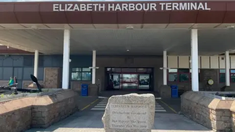 BBC A picture of the entrance to Elizabeth Terminal. It is a cream-coloured building with a brown sign at the entrance which reads Elizabeth Harbour Terminal.
