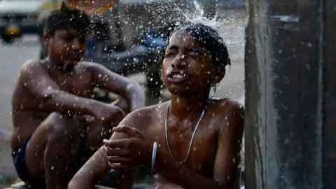 AFP Two shirtless boys relax under a water tap in India, with the front boy's eyes closed as a stream of water falls on his head.