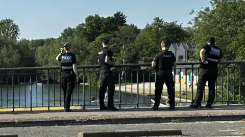 Four police officers stand on Donnington Bridge on 28.5.26, looking over railings at the river