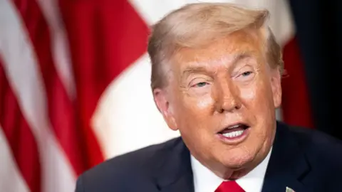 EPA US President Donald Trump speaks in a white shirt, red tie and black suit jacket in front of a red and white flag