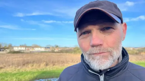 ANDREW TURNER/BBC Russell Biggs stands next to the Gaywood River and Russett Meadows