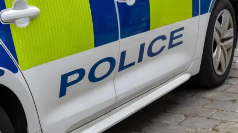 The side of a police car. It is yellow and blue with the word 'police' written on it. 
