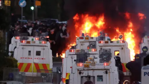 PA Media Rioters have set fire to wheelie bins and removed a garden fence to use as a shield against a police water cannon on Antrim Road, at the Sandyknowes roundabout in Newtownabbey.
