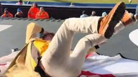Football fan lying on the England flag as he rolls off the stand at a football game