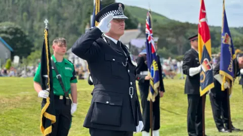 Foster in his police uniform saluting while standard bearers line the walkway behind.