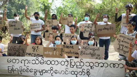 Protesters hold up signs and hold up a three-fingered salute in Thailand