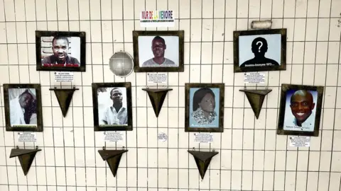 Portraits of seven people are displayed on the wall of an office – 'Wall of Memory' is written in French above the pictures.